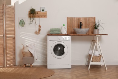 Photo of Laundry room interior with modern washing machine and stylish vessel sink on wooden countertop