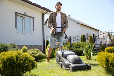 Photo of Man cutting green grass with lawn mower in garden