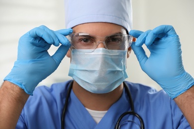 Photo of Doctor in protective mask, glasses and medical gloves against light background
