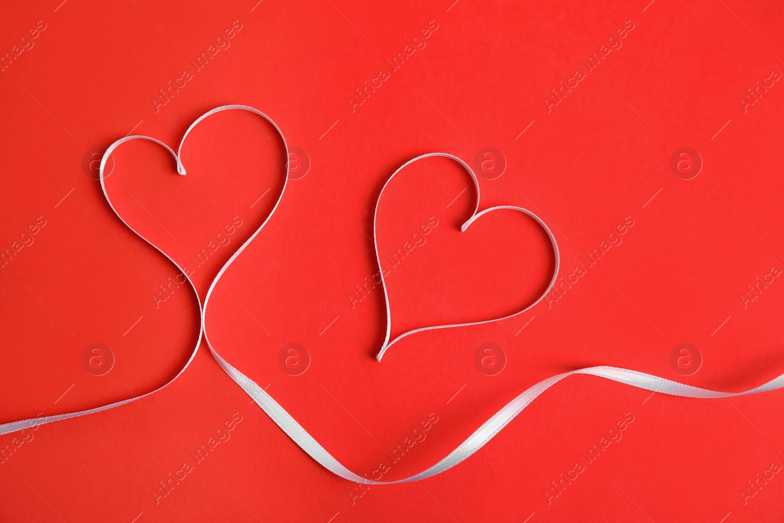Photo of Hearts made of white ribbon on red background, flat lay. Valentine's day celebration