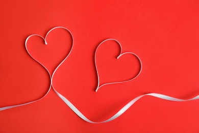 Photo of Hearts made of white ribbon on red background, flat lay. Valentine's day celebration