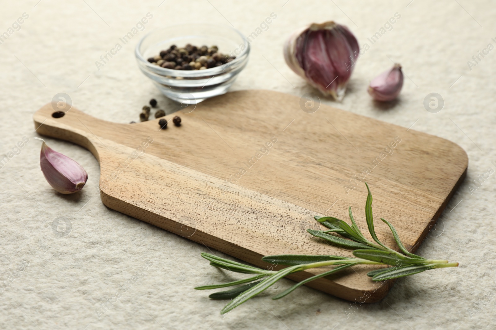 Photo of Cutting board, garlic, pepper and rosemary on white textured table. Space for text