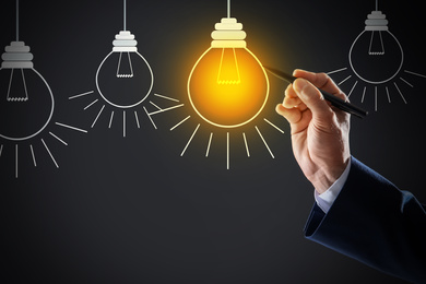 Image of Idea concept. Businessman drawing glowing light bulb on virtual screen, closeup