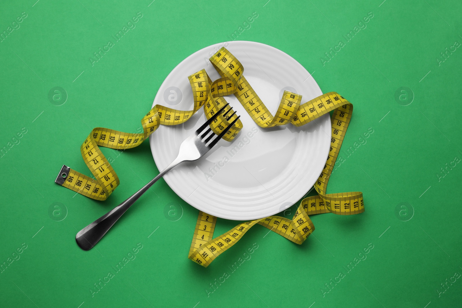 Photo of Plate, measuring tape and fork on green background, top view. Diet concept