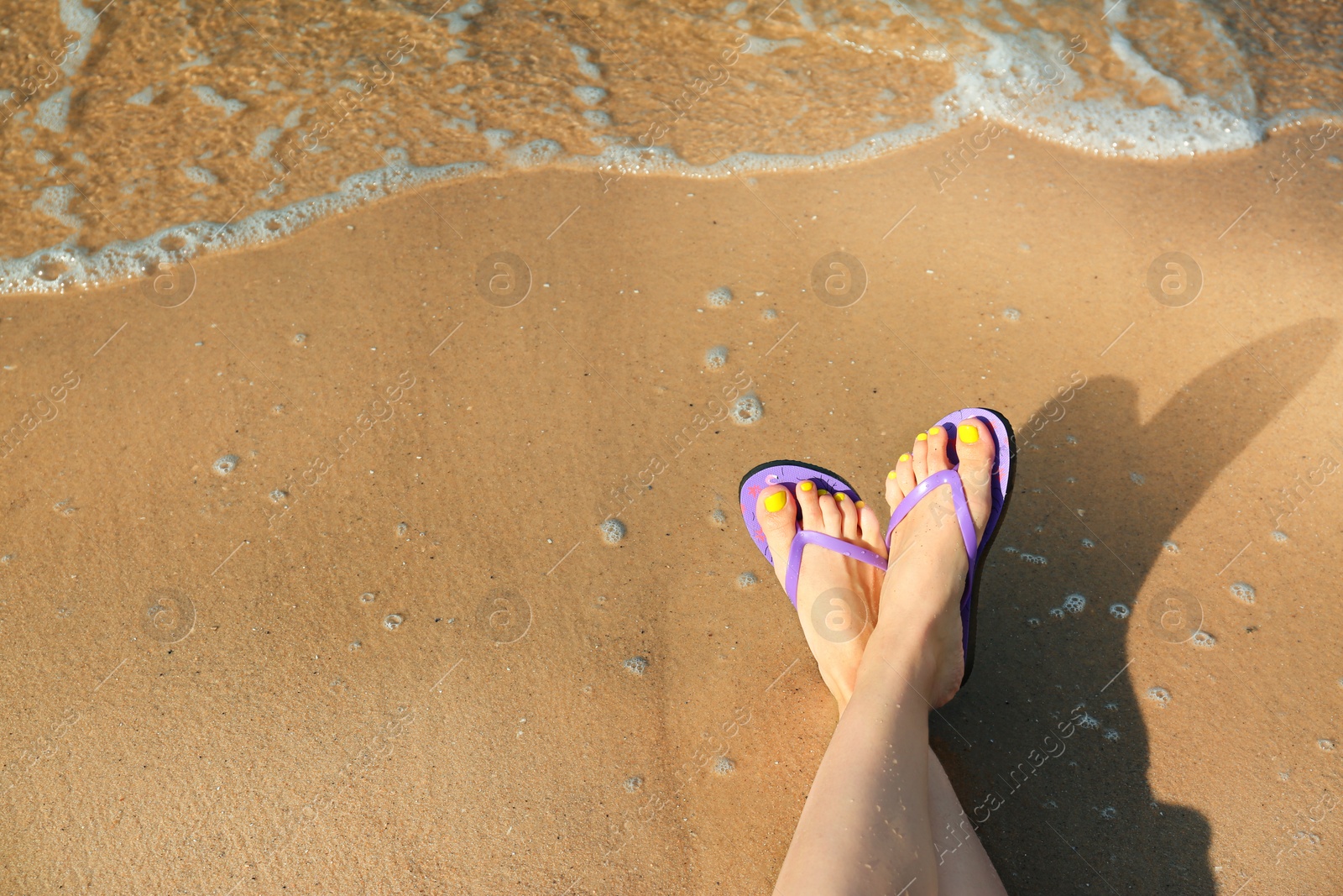 Photo of Closeup of woman with flip flops on sand near sea, space for text. Beach accessories