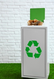 Overfilled trash bin near brick wall indoors. Recycling concept