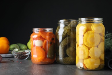 Photo of Jars of tasty pickled vegetables on grey table