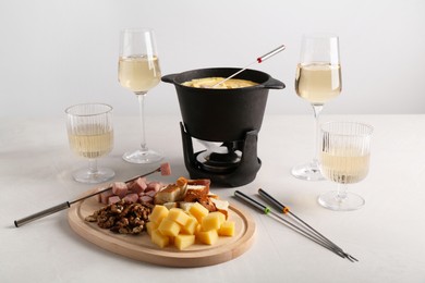 Fondue pot with tasty melted cheese, forks, wine and different snacks on white table