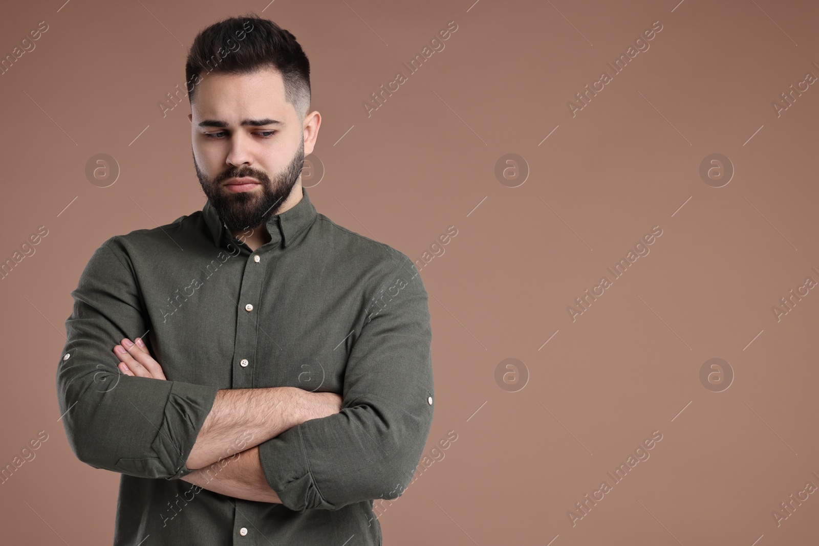 Photo of Portrait of sad man with crossed arms on brown background, space for text