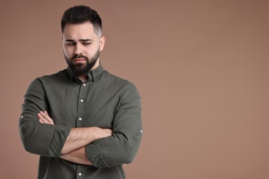 Photo of Portrait of sad man with crossed arms on brown background, space for text