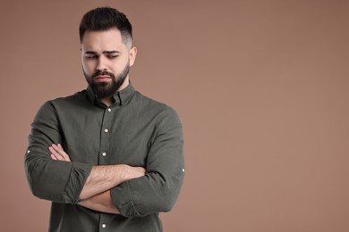 Portrait of sad man with crossed arms on brown background, space for text