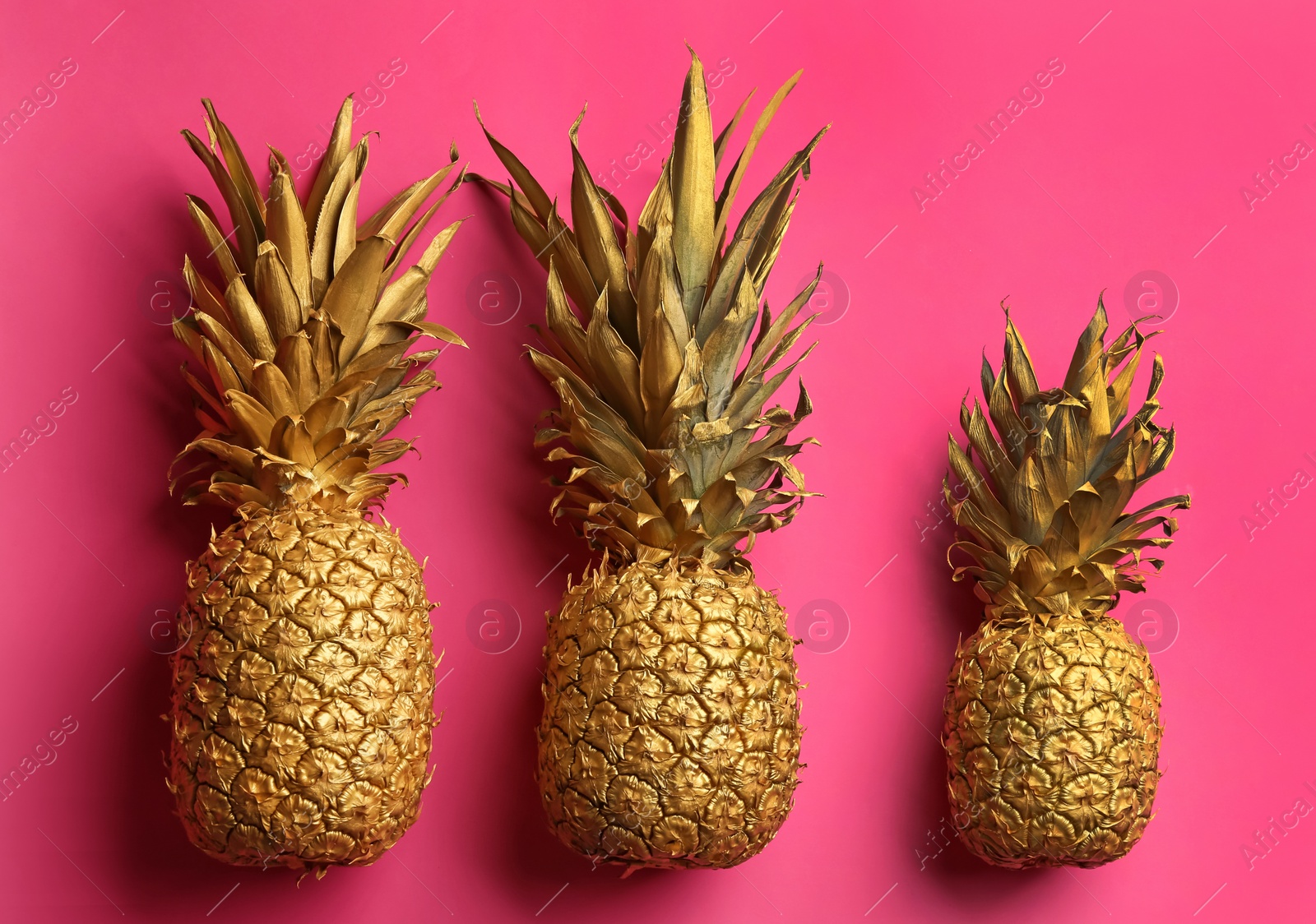 Photo of Painted golden pineapples on pink background, flat lay. Creative concept