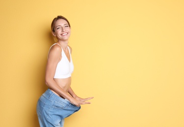 Photo of Young slim woman in old big jeans showing her diet results on color background