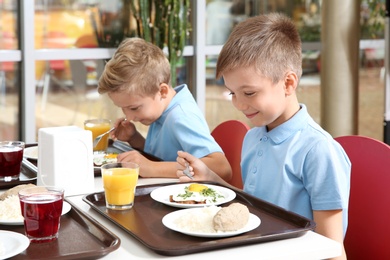 Photo of Cute children at table with healthy food in school canteen