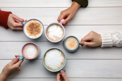 Photo of People holding different cups with aromatic hot coffee at white wooden table, top view