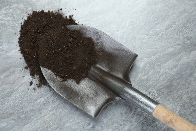 Photo of Metal shovel with fertile soil on gray textured surface, top view