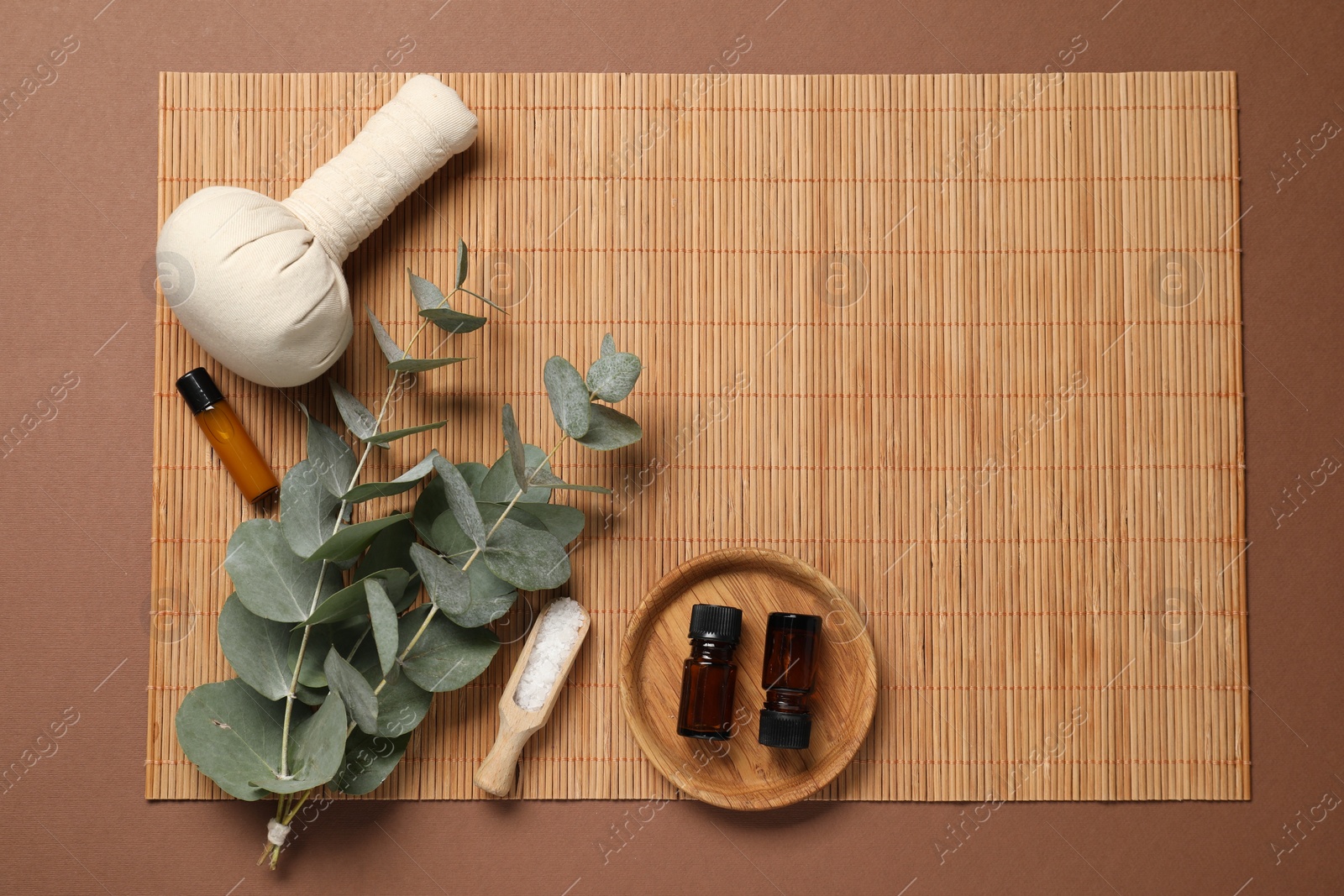 Photo of Different aromatherapy products and eucalyptus branches on brown background, flat lay