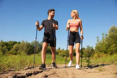 Happy couple practicing Nordic walking with poles outdoors on sunny day, low angle view