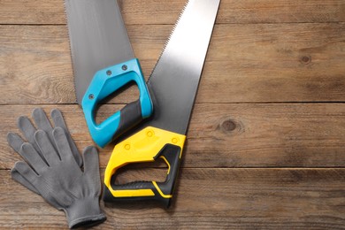 Photo of Saws with colorful handles and gloves on wooden background, flat lay. Space for text