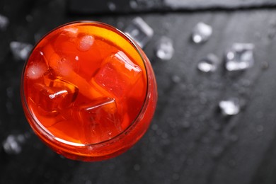 Photo of Glass of tasty Aperol spritz cocktail with orange slices and ice cubes on dark gray table, top view. Space for text
