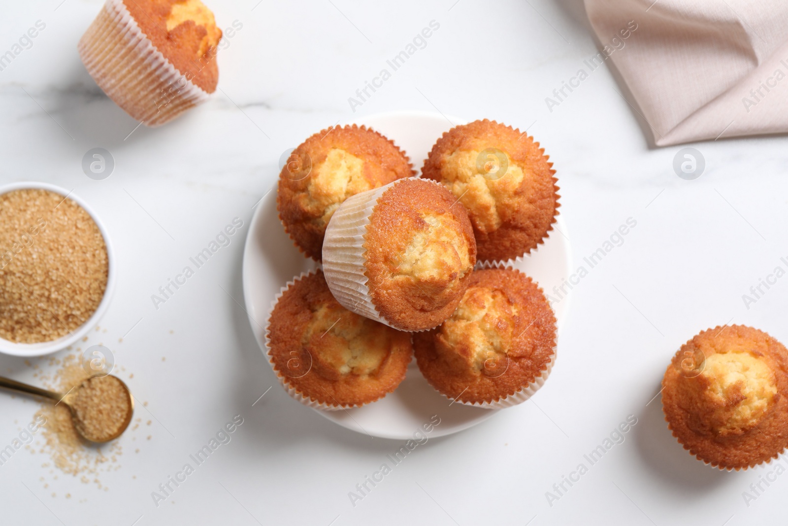 Photo of Delicious sweet muffins and brown sugar on white marble table, flat lay