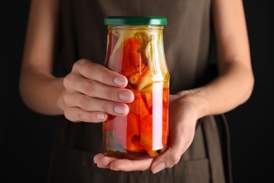 Woman holding jar with pickled bell peppers against black background, closeup