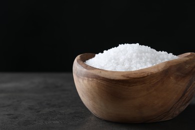 Photo of Natural salt in wooden bowl on dark grey table, closeup. Space for text