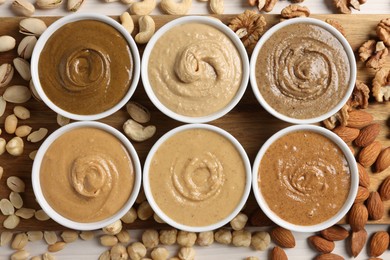 Photo of Many tasty nut butters in bowls and nuts on white table, flat lay