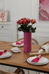 Color accent table setting. Plates, cutlery, pink napkins and vase with beautiful roses in dining room