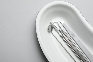 Photo of Kidney shaped tray with set of dentist's tools on light grey background, top view. Space for text