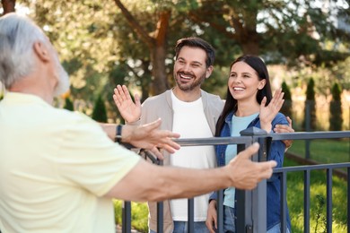 Photo of Friendly relationship with neighbours. Happy couple greeting senior man near fence outdoors