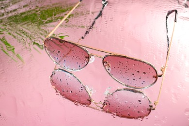 Photo of Stylish sunglasses with water drops on glass table