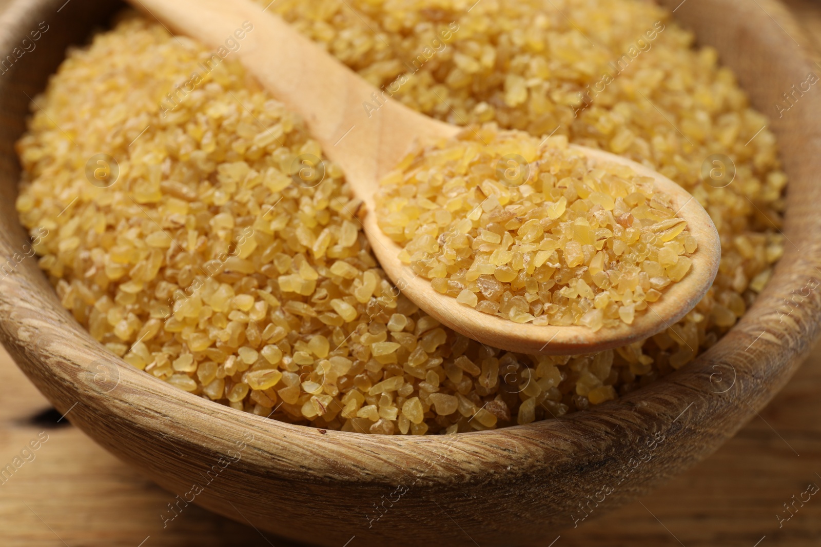 Photo of Bowl and spoon with raw bulgur on table, closeup