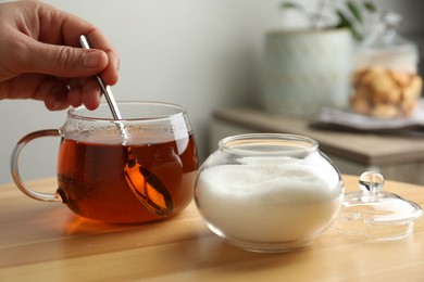 Woman stirring sugar in tea at wooden table indoors, closeup