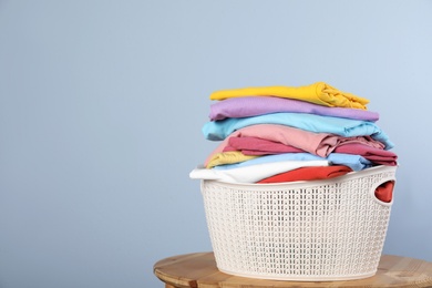 Photo of Plastic laundry basket with clean clothes on stool against color background. Space for text