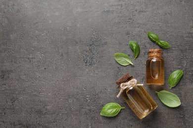 Photo of Bottles of essential basil oil and fresh leaves on grey table, flat lay. Space for text