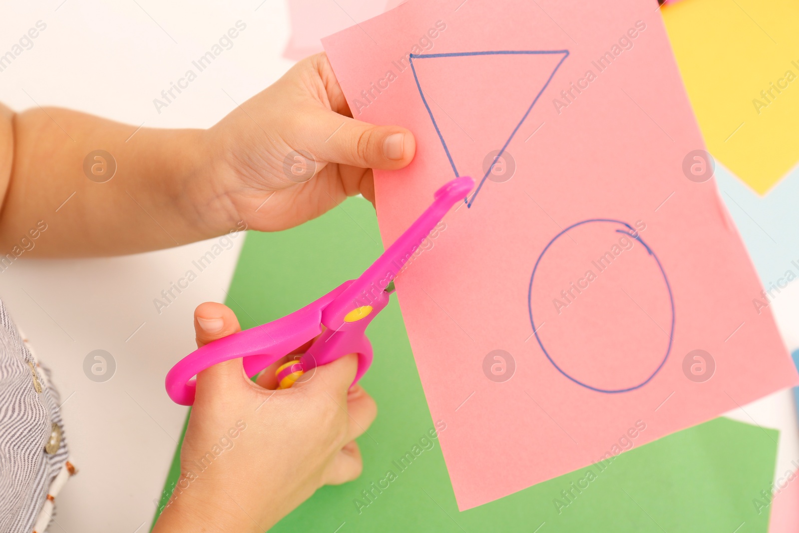 Photo of Little girl cutting color paper with scissors at table, above view