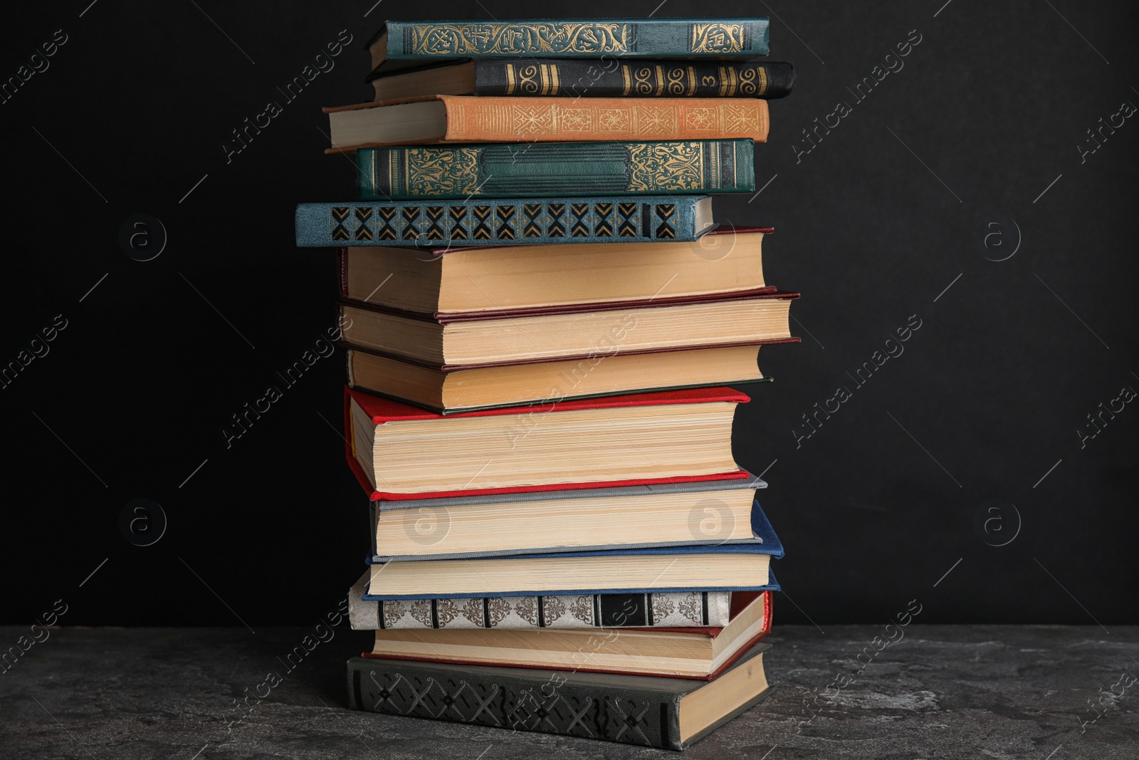 Photo of Stack of hardcover books on grey stone table against black background