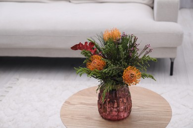 Vase with bouquet of beautiful leucospermum flowers on wooden table in living room