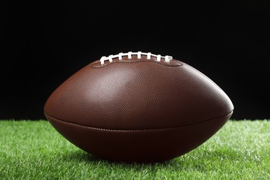 Photo of American football ball on green grass against black background