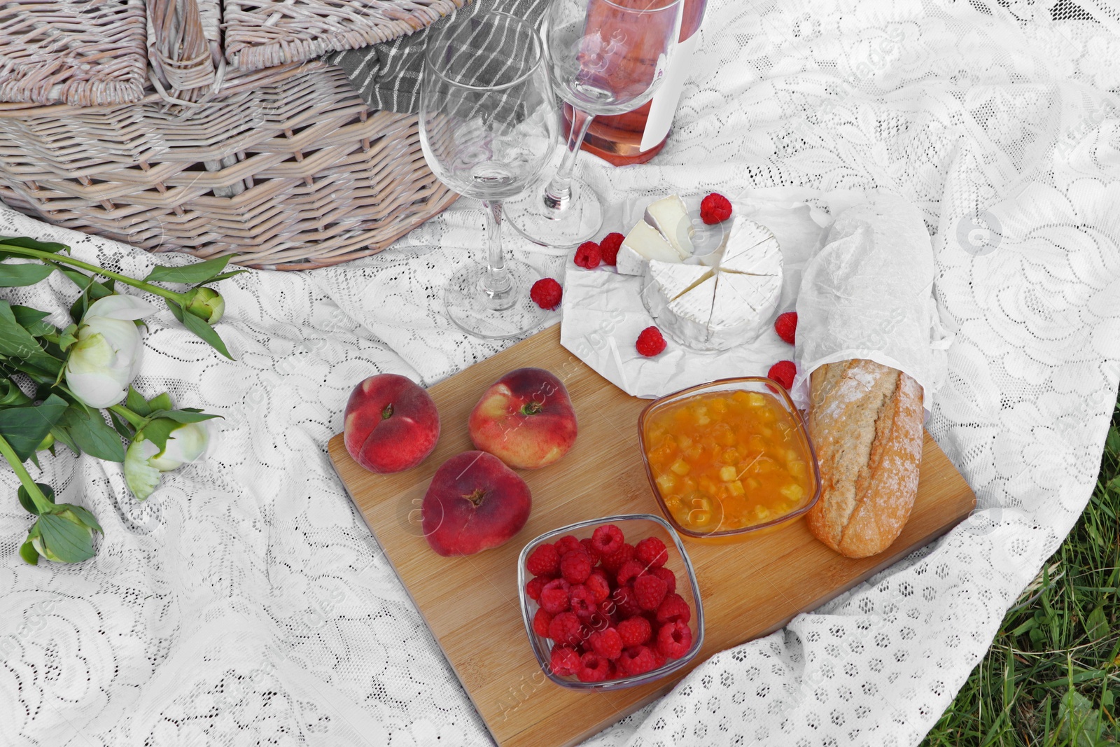 Photo of Picnic blanket with tasty food, flowers, basket and cider on green grass outdoors