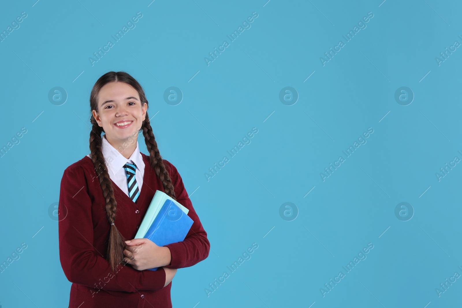 Photo of Teenage girl in school uniform with books on light blue background, space for text