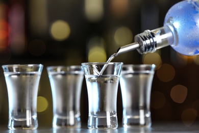 Pouring vodka from bottle into shot glass on bar counter