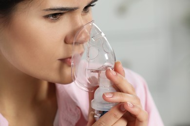 Photo of Sick young woman using nebulizer on blurred background, closeup. Space for text