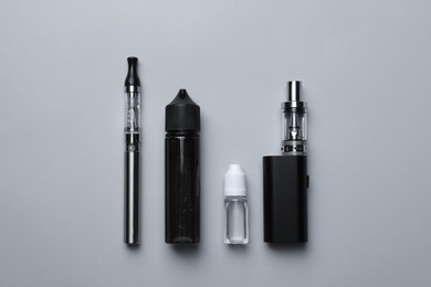 Photo of Electronic cigarettes and liquid solution on light background, flat lay