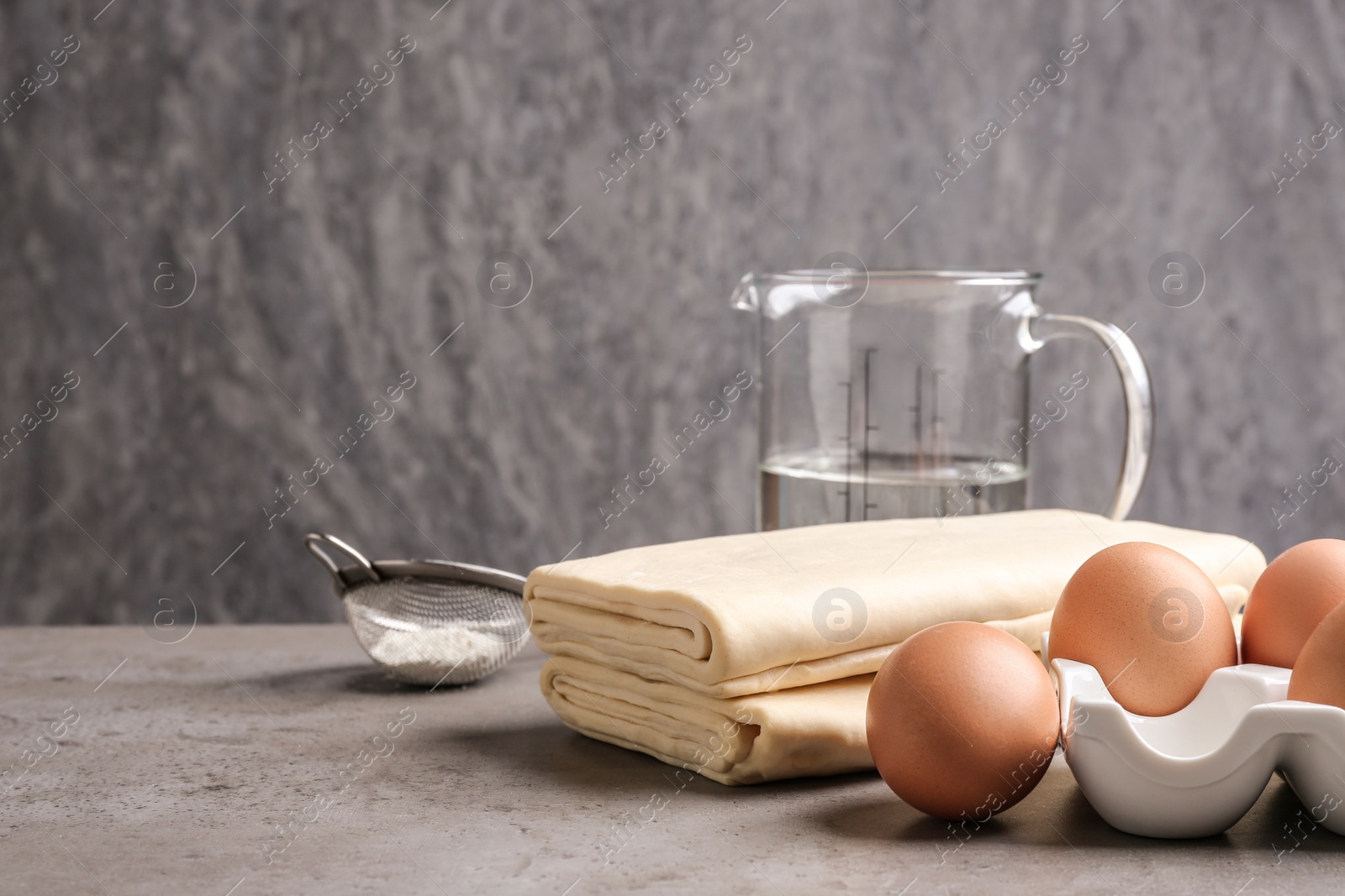 Photo of Composition with fresh dough on table against grey background, space for text. Puff pastry