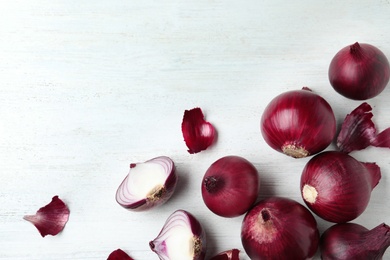 Photo of Ripe red onions and peels on white wooden table, top view with space for text