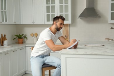 Photo of Handsome man with notebook sitting on stool in kitchen