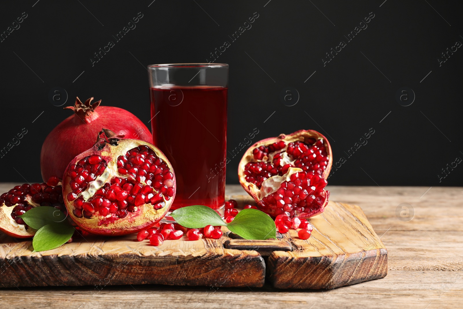 Photo of Glass of pomegranate juice and fresh fruits on wooden board against black background, space for text