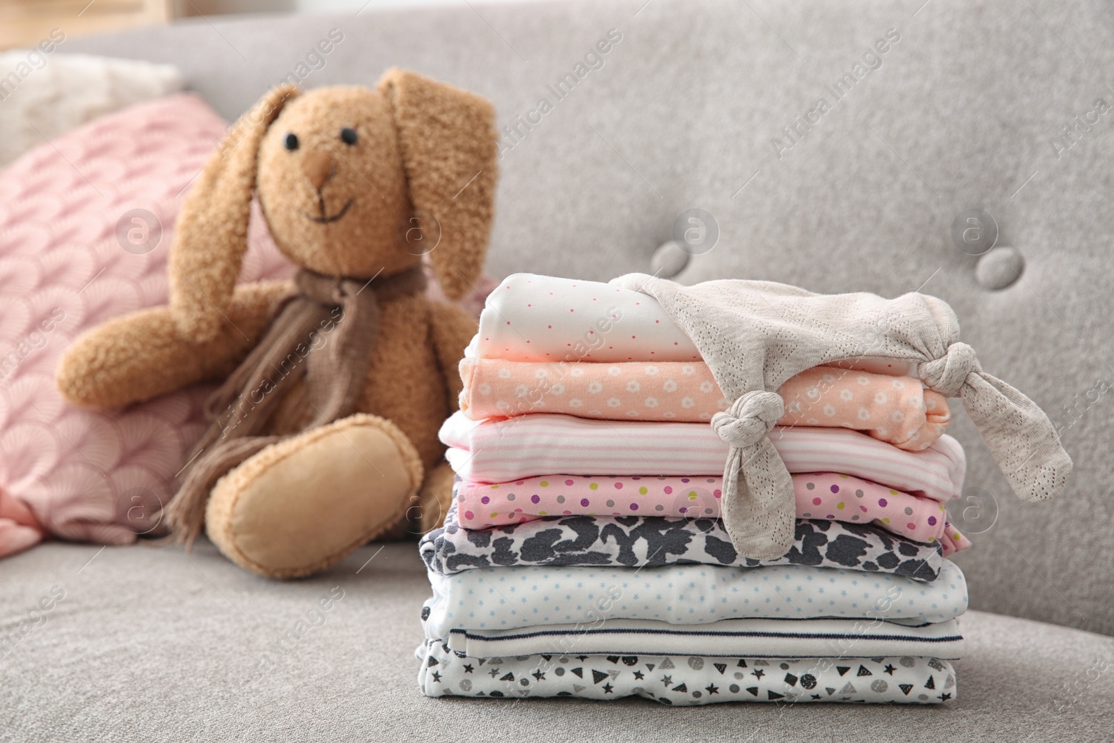 Photo of Toy bunny and stack of stylish child clothes on sofa